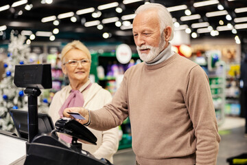 An old man in paying on self-service cash register at the supermarket.