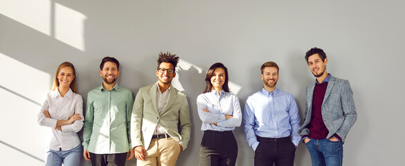 Successful smiling team of employees standing near gray wall. Diverse enthusiastic young colleagues...