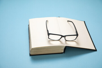 Eyeglasses and book on the blue background.