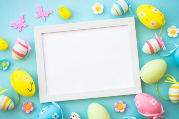 Easter greeting card on blue. Colored easter eggs with decorations and white frame for text. Flat lay with copy space.