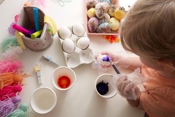 Children's hands paint Easter eggs with elements of spring decor table top view