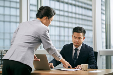 asian business manager reviewing report with subordinate in office