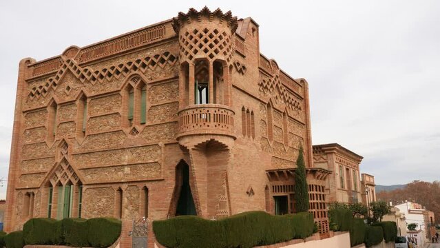 View of historic factory manager house in center of Colonia Guell - red brick mansion with lacy walls. Tourist attractions in Catalonia, Spain