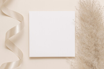 Minimal blank paper sheet card with ribbon and pampas grass on beige neutral background, top view,...