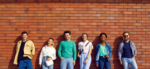 Six diverse relaxed young people in clothes for everyday wear and leisure. Group portrait of handsome men and beautiful women in shirts, tees and jumpers leaning on street wall. Casual fashion concept © Studio Romantic