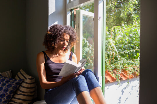 Woman reading book on window sill