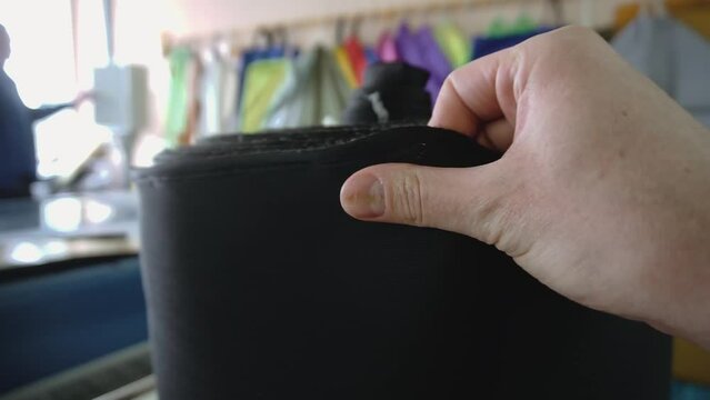 Man touches black dense fabric on roll in sewing workshop