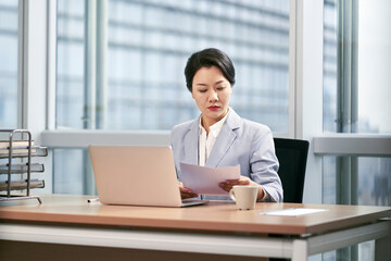 young asian businesswoman working in modern office looking at report using laptop computer