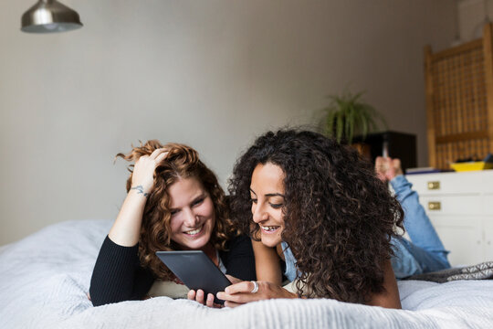 Two women lying on front on bed and using e-reader