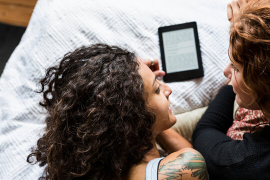 Two women lying on front on bed and using e-reader