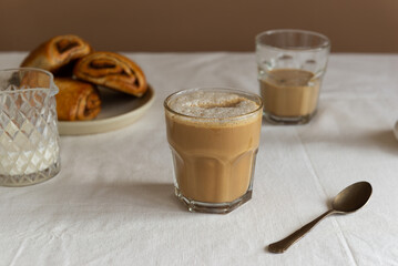 Homemade coffee cappuccino in a glass with cinnamon buns on table, rustic style.