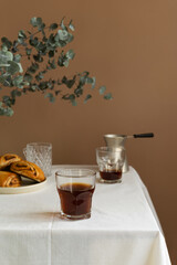 Fresh coffee Americano in a glass with cinnamon buns on table, rustic style.