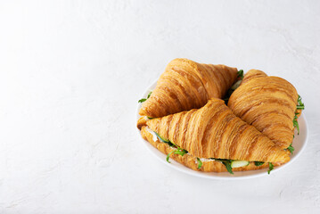 Crispy croissants sandwiches with salmon fish, cream cheese, cucumber and arugula on a plate.