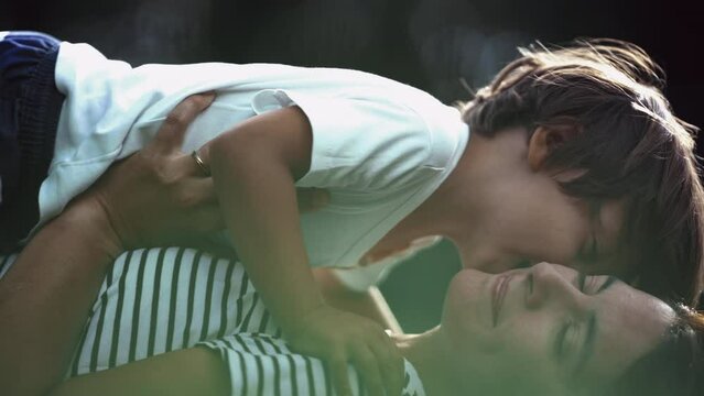 Child kissing mother on cheek outside in nature. Little boy and parent relationship showing love and affection. Motherhood concept