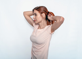 Naklejka premium Young attractive woman fixing hair while holding hands behind head. Light T-shirt. White background.