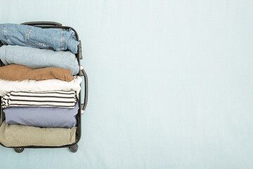 An open suitcase with neatly folded konmari clothes vertically. The concept of packing clothes for a trip, vacation or business trip. Copy space, top view, minimalism