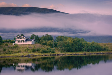 Fototapeta na wymiar House by a fairy tale lake with the mist at sunset, in the Vesteralen islands, Norway