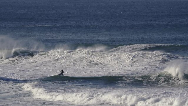 A jetski driver and a surfer ride the foamy waves into the open sea