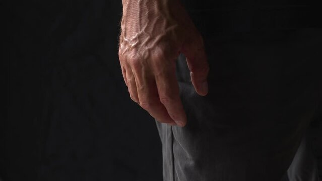 Close-up of palm of an mature man with bulging veins is tightly clenched into a fist in rage on a black background. Consept aggression and ready to fight.