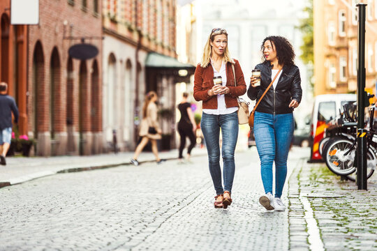 Two women with coffee cups walking on city street