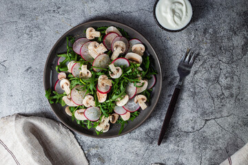 Vegetarian salad of fresh arugula, radish and mushrooms in a plate on a dark background