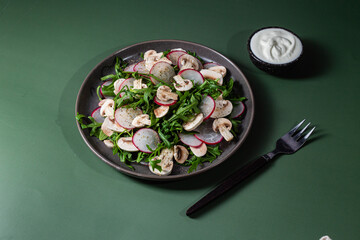 Vegetarian salad of fresh arugula, radish and mushrooms in a plate on a dark background