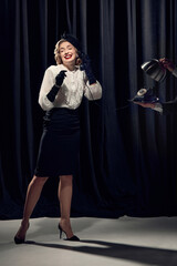 Adorable woman wearing vintage clothes holding phone and talking with smiling over dark background