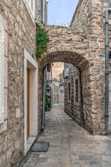 Arched passage on a narrow street in the Old Town Stari Grad in Budva, Montenegro. Outdoor view of ancient buildings with stone walls, vertical