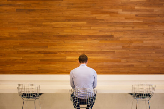 Rear view of man sitting on chair in front of wooden wall