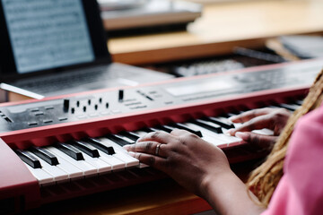 Close-up of African American girl using sheet music and learning to play synthesizer at table