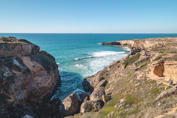Breathtaking cliffs with crashing waves in the afternoon sun on the Atlantic coast near Vila Nova de Milfontes, Odemira, Portugal. In the footsteps of Rota Vicentina. Fisherman trail. Clear blue sky