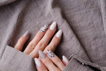 A woman's hand with a beautiful manicure holds a beige fabric. Autumn trend, beige color polishing with leopard pattern on nails with gel polish, shellac.