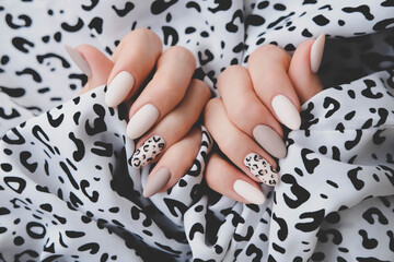 A woman's hand with a beautiful manicure holds a fabric with a leopard print. Autumn trend, beige...