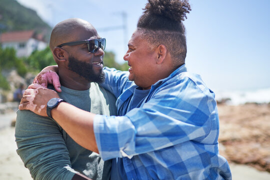 Affectionate gay male couple hugging face to face on sunny beach