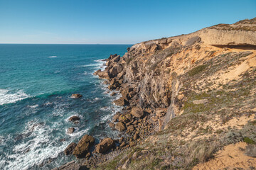 Breathtaking cliffs with crashing waves in the afternoon sun on the Atlantic coast near Vila Nova de Milfontes, Odemira, Portugal. In the footsteps of Rota Vicentina. Fisherman trail. Clear blue sky