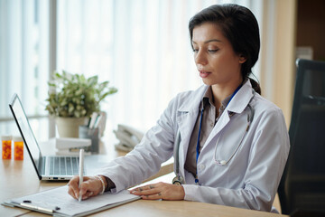Physician writing out prescription after having telemedicine session with patient