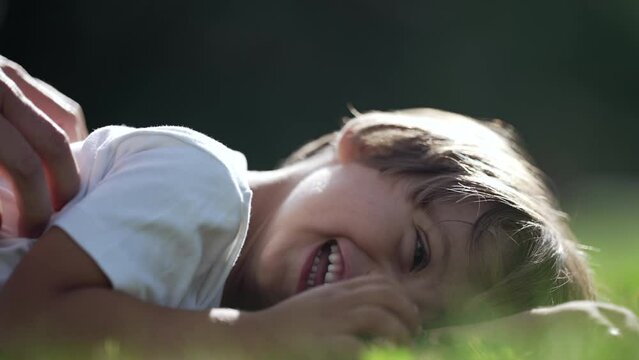 Joyful child happy expression laid on grass in beautiful sunny day. One young boy laughing and smiling. Kid being tickled
