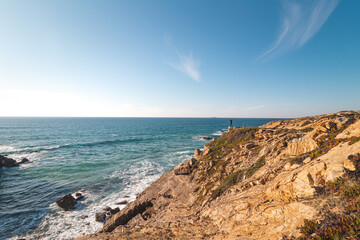 Hiker enjoys the breathtaking cliffs with a pebble beach in the afternoon sun on the Atlantic coast at Vila Nova de Milfontes, Odemira, Portugal. In the footsteps of Rota Vicentina. Fisherman trail