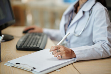Cropped image of physician checking patients medical history in database on computer and taking notes