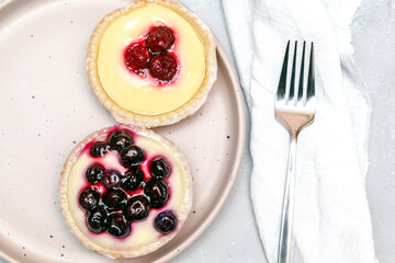 Delicious red raspberry strawberry, blueberry whipped creamy tartlets,cakes.gourmet confection dessert on plate with napkin.sweet tasty pastry baked pie cheesecake with ripe berries on gray table