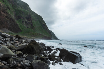 Rocky beach on Madeira Island, green volcanic cliffs at moody weather