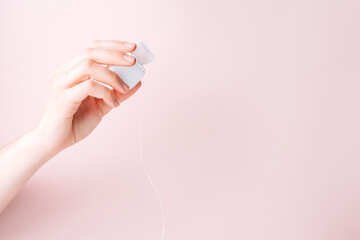 Dental floss in a female hand against a pink background.