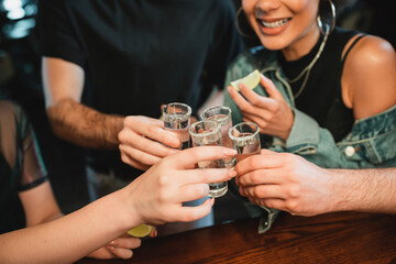 cropped view of multiethnic people holding tequila shots with salt on glasses in bar. - obrazy, fototapety, plakaty
