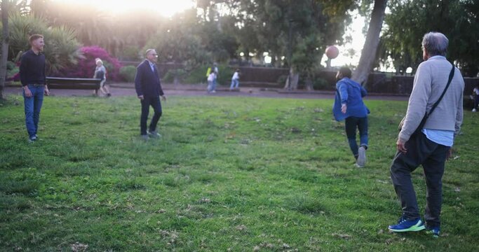 Group of multi generational men having fun together playing football at city park 