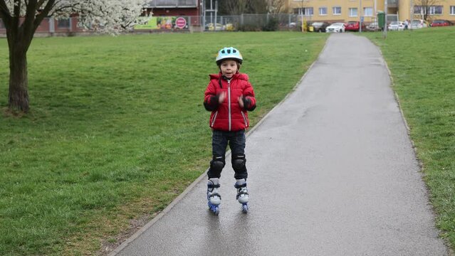 Little child, preschool boy in protective equipment and rollers blades, riding on walkway in park