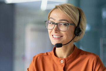 Close-up portrait of young beautiful blonde woman at workplace, call center worker smiling and...