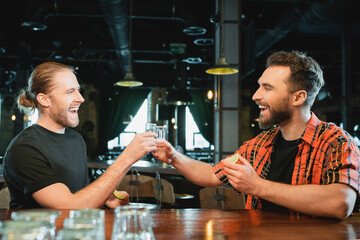 cheerful male friends holding lime and clinking tequila shots in bar.