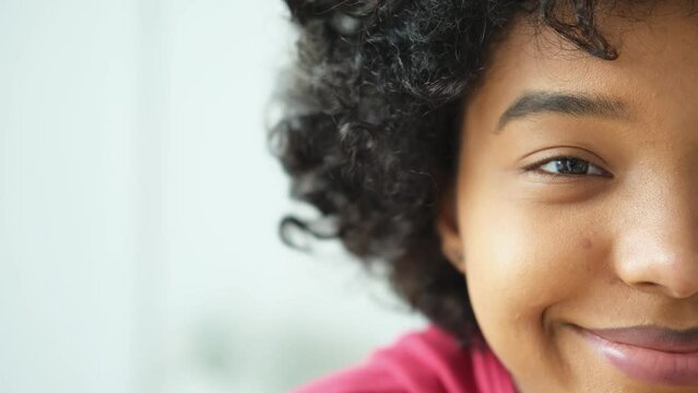 Beautiful african american happy girl with afro hairstyle smiling. Young woman eye half face portrait close up. Young african woman with curly hair laughing. Natural beauty happy people concept