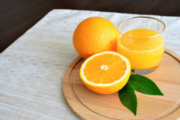 A glass of orange juice with two oranges on a wooden plate isolated, close-up