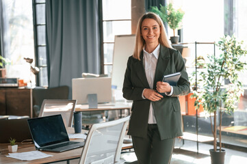 Standing and smiling. Young beautiful woman in formal clothes is working in the office